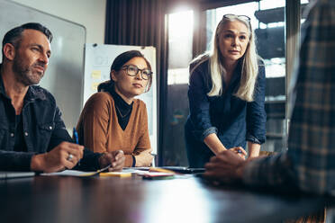 Group of business people listening to ideas of young colleague in meeting room. Diverse business team brainstorming in meeting room. - JLPSF22766