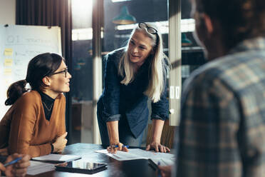 Ältere Geschäftsfrau, die ihrem Team in einem Sitzungssaal geschäftliche Angelegenheiten erklärt. Reife Managerin, die in einer Sitzung mit Kollegen eine neue Strategie plant. - JLPSF22768