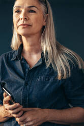 Portrait of confident senior woman holding phone looking away. Woman with white hair in casuals. - JLPSF22784