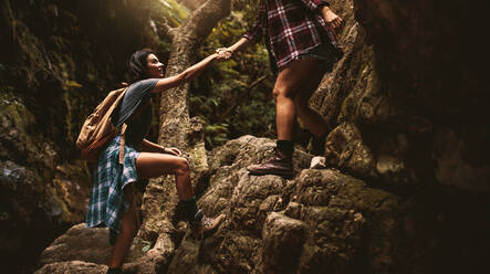 Frau hält die Hand einer Freundin beim Klettern auf einen Felsen während einer Bergwanderung. Frau hilft Freundin bei einer Wanderung durch extremes Gelände in den Bergen. - JLPSF22806