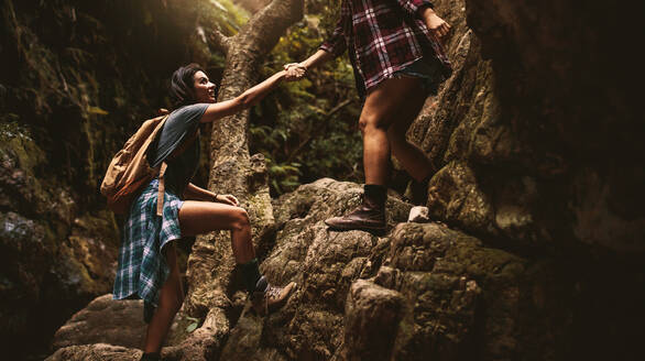 Frau hält die Hand einer Freundin beim Klettern auf einen Felsen während einer Bergwanderung. Frau hilft Freundin bei einer Wanderung durch extremes Gelände in den Bergen. - JLPSF22806