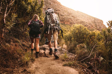 Rückansicht eines jungen Mannes und einer jungen Frau, die durch einen Bergpfad wandern. Junge Leute mit Rucksäcken wandern in den Bergen. - JLPSF22824