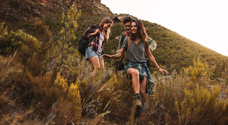 Group of friends walking through a rough terrain. Two women and a man hiking on a rocky mountain trail. - JLPSF22831