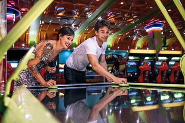 Glückliches Paar, das als Team in einer Spielhalle Airhockey mit Münzen spielt. Freunde, die in einer Spielhalle Airhockey spielen. - JLPSF22836