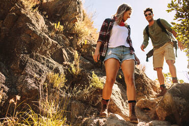 Tiefblick auf einen jungen Mann und eine Frau, die über einen felsigen Bergpfad wandern. Ein Paar wandert durch extremes Terrain. - JLPSF22848