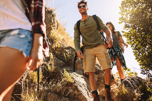 Junger Mann mit zwei Freundinnen, die durch einen felsigen Pfad wandern. Freunde wandern auf einem felsigen Bergpfad. - JLPSF22849