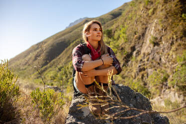 Wanderin auf einem Felsen sitzend mit Blick auf die Berge. Frau ruht sich während einer Wanderung in den Bergen aus. - JLPSF22853