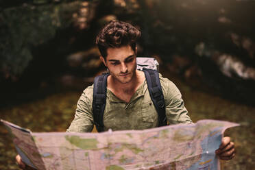 Hübscher junger Mann mit Rucksack, der beim Wandern in den Bergen auf die Karte schaut, um den Weg zu finden. Männlicher Wanderer, der eine Karte benutzt, um das Ziel zu finden. - JLPSF22858