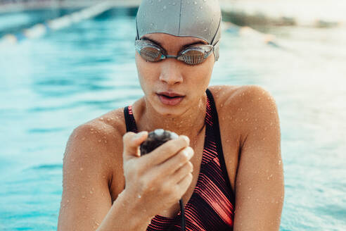Eine Schwimmerin prüft nach einer Runde die Stoppuhr. Eine Frau in Badekleidung bereitet sich auf einen Schwimmwettbewerb vor. - JLPSF22878