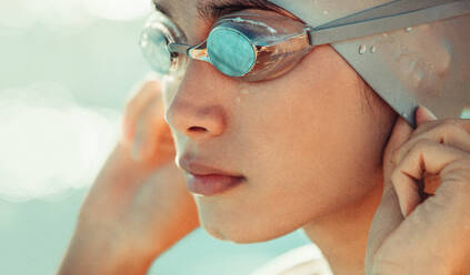 Nahaufnahme einer jungen Schwimmerin, die ihre Badekappe anpasst. Professioneller Schwimmsportler mit Badekappe und Schwimmbrille. - JLPSF22887