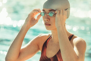 Porträt einer Frau mit Schwimmbrille und Badekappe in der Nähe des Schwimmbeckens. Eine Schwimmerin passt ihre Schwimmbrille vor dem Schwimmen an. - JLPSF22890