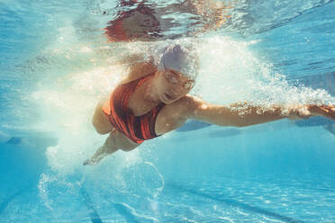 Unterwasseraufnahme einer Frau beim Kraulen im Sportbecken. Eine fitte Sportlerin übt im Schwimmbad. - JLPSF22895