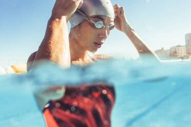 Nahaufnahme einer jungen Schwimmerin im Schwimmbad, die ihre Schwimmbrille einstellt. Professionelle Schwimmerin macht eine Pause beim Training im Freibad. - JLPSF22896