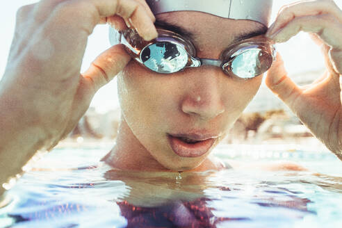 Nahaufnahme einer jungen Schwimmerin im Schwimmbad, die ihre Schwimmbrille einstellt und tief einatmet. Professionelle Schwimmerin macht eine Pause beim Schwimmen im Freibad. - JLPSF22897