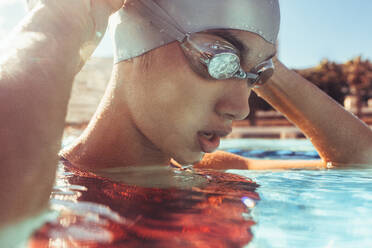 Nahaufnahme einer jungen Schwimmerin im Schwimmbad, die ihre Schwimmbrille einstellt. Professionelle Schwimmerin macht eine Pause während des Schwimmtrainings. - JLPSF22899
