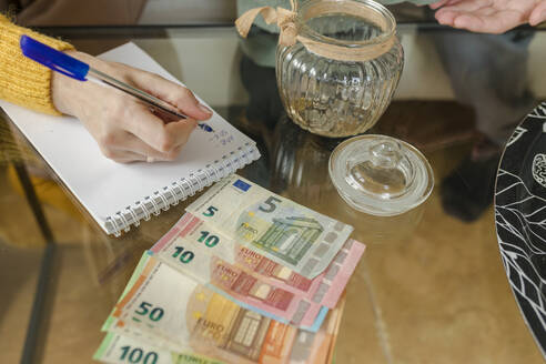 Hand einer Frau, die auf einen Notizblock schreibt und Geld zu Hause zählt - VIVF00092