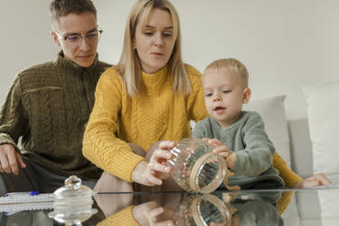 Mann und Frau mit Sohn halten Glas im Wohnzimmer zu Hause - VIVF00095