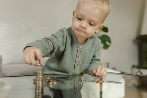 Boy counting coins on table at home - VIVF00098