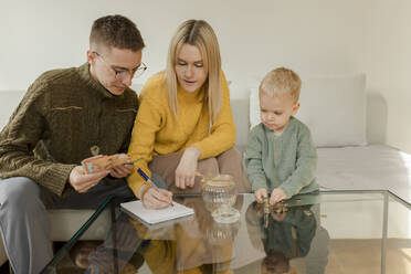 Junger Mann und Frau mit Sohn zählen Geld auf dem Tisch zu Hause - VIVF00099