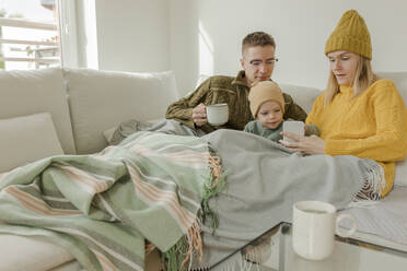 Junges Paar mit Sohn benutzt Smartphone auf dem Sofa zu Hause - VIVF00104