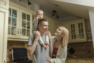 Happy woman with man carrying son on shoulders in kitchen at home - VIVF00106