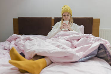 Junge Frau mit Kaffeetasse auf dem Bett sitzend zu Hause - VIVF00124