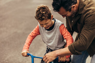 Mann hält das Fahrrad, während sein Sohn das Fahren lernt. Junge freut sich auf das Fahrradfahren. - JLPSF22900