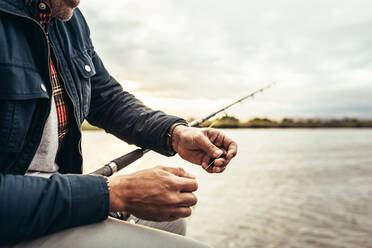 Ausschnitt einer Person, die ihre Angelrute für den Fischfang vorbereitet. Ein Mann legt einen Köder an seine Angelrute, um einen Fisch zu fangen. - JLPSF22919