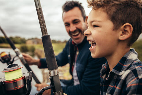 Close up of a smiling man fishing along with his son in a lake. Smiling man looking at his son enjoying fishing on a pleasant day. - JLPSF22930