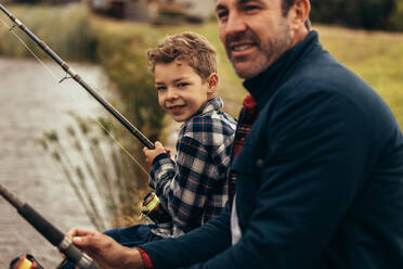Ausschnitt eines Mannes, der mit seinem Kind am Ufer eines Sees sitzt und eine Angel in der Hand hält; Vater und Sohn beim Angeln als Freizeitbeschäftigung. - JLPSF22933