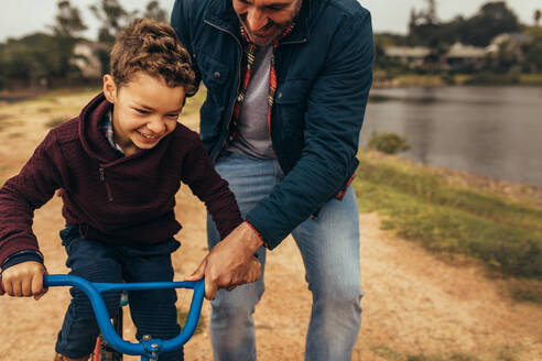 Ein Mann hilft seinem Sohn beim Fahrradfahren. Ein aufgeregtes Kind lernt Fahrradfahren, während sein Vater das Fahrrad vor einem Sturz bewahrt. - JLPSF22937