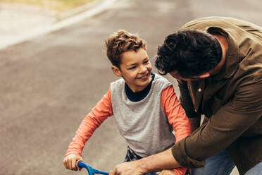 Vater, der seinem Sohn das Fahrradfahren beibringt. Mann, der seinem Sohn hilft, Fahrradfahren zu lernen. - JLPSF22940