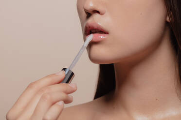 Close up of woman applying lip gloss. Cropped shot of korean girl putting on makeup on her lips against beige background. - JLPSF22951