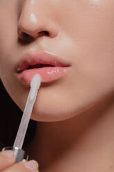 Close up of woman applying transparent lip gloss with applicator. Cropped shot of girl doing makeup on her lips. - JLPSF22953