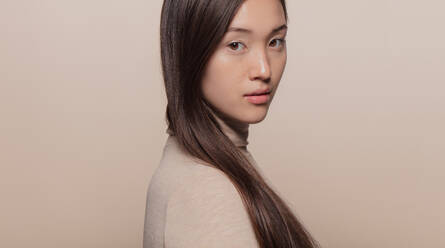 Porträt einer schönen asiatischen Frau mit braunen Haaren vor beigem Hintergrund. Koreanisches weibliches Modell schaut in die Kamera. - JLPSF22965