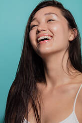 Schönes asiatisches Mädchen lachend gegen blauen Hintergrund. Schönes Gesicht des Mädchens mit frischer gesunder Haut. - JLPSF22971