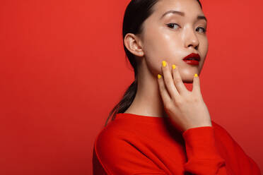 Porträt einer attraktiven jungen asiatischen Frau mit schönem Make-up auf rotem Hintergrund. Asiatisches weibliches Modell mit rotem Top und Lippenstift. - JLPSF22979
