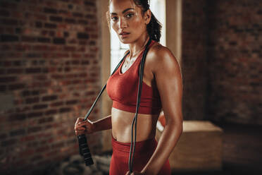 Fit and healthy woman standing at gym with skipping rope. Sportswoman resting after workout. - JLPSF23044