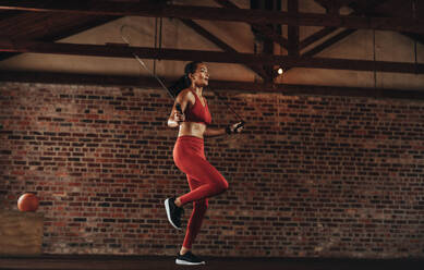 Healthy woman exercising with skipping rope at fitness studio. Sportswoman doing jumping rope workout at gym. - JLPSF23051