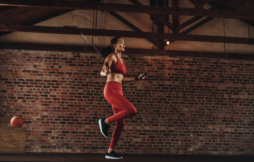 Gesunde Frau trainiert mit Springseil im Fitnessstudio. Sportlerin macht Seilspringen im Fitnessstudio. - JLPSF23051