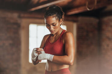 Junge Frau mit muskulösem Körper, die sich auf das Boxtraining im Fitnessstudio vorbereitet. - JLPSF23054