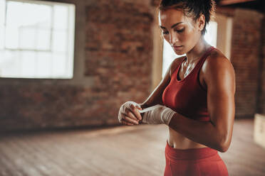 Gesunde junge Boxerin, die einen Gurt am Handgelenk trägt. Muskulöse Frau, die sich im Fitnessstudio auf das Boxtraining vorbereitet. - JLPSF23056