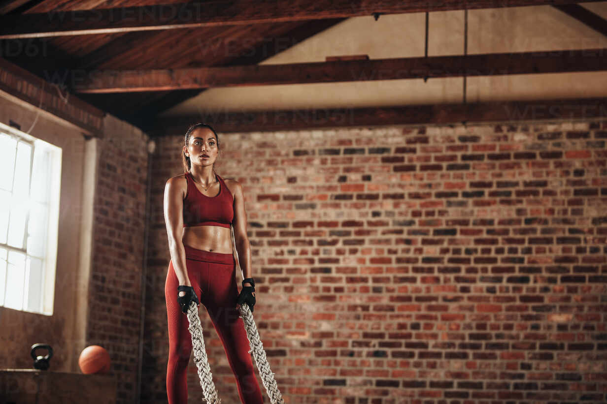 Young woman doing strength training using battle ropes at the gym
