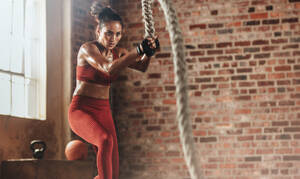 Eine fitte und muskulöse Frau trainiert mit Kampfseilen im Fitnessstudio. Eine Sportlerin macht ein Kampfseiltraining im Fitnessstudio. - JLPSF23067