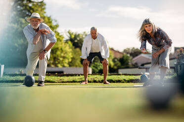 Ebenerdige Aufnahme eines älteren Mannes und einer älteren Frau, die auf einer Wiese Boule spielen, mit einem unscharfen Boule-Spiel im Vordergrund. Ein älterer Mann und eine ältere Frau spielen miteinander Boule. - JLPSF23074