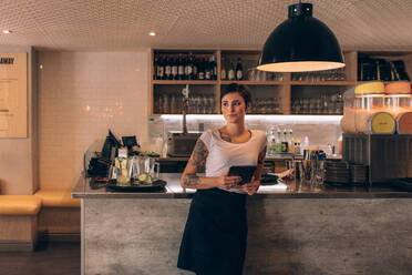 Porträt einer schönen jungen Frau, die an der Theke eines Cafés steht, mit einem digitalen Tablet. - JLPSF23095