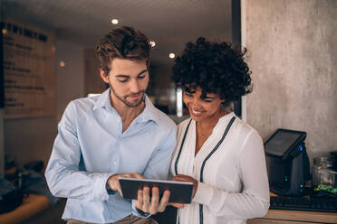 Zwei Restaurantgeschäftspartner stehen zusammen und schauen auf ein digitales Tablet. Mann und Frau benutzen ein digitales Tablet in einem Café. - JLPSF23096