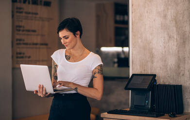 Junge Frau mit Laptop in ihrem Restaurant. Café-Besitzerin mit Laptop. - JLPSF23107