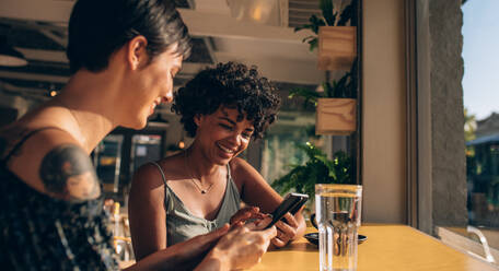 Zwei junge Frauen, die in einem Café sitzen und ihre Handys benutzen, Freundinnen, die in einem Café soziale Kontakte pflegen. - JLPSF23112