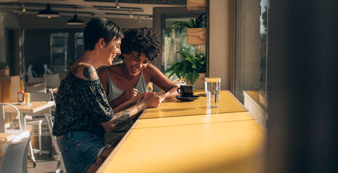 Zwei Frauen sitzen in einem Café und benutzen ein Smartphone. Freundinnen schauen auf ihr Handy und lächeln. - JLPSF23113